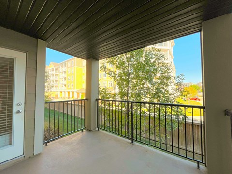 A balcony with a metal railing and a view of a green lawn and buildings.