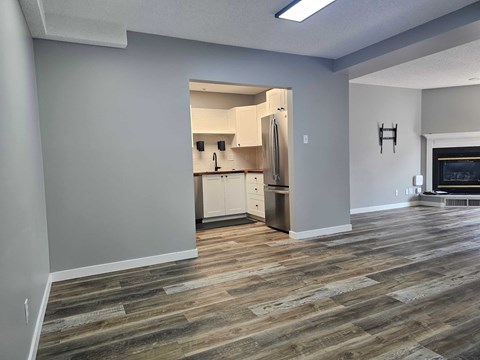 A kitchen with a refrigerator, oven, and cabinets is visible through an open doorway.