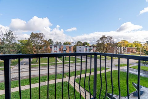 A view from a balcony overlooking a grassy area and a road with houses in the distance.