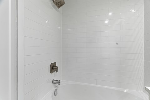 A white tiled shower with a shower head and faucet.