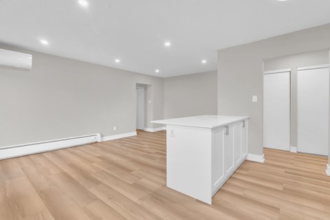 A white kitchen island sits in the middle of a room with wooden floors and white walls.