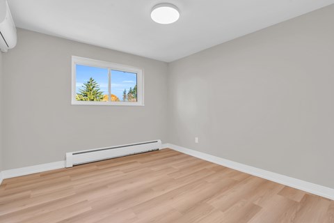 A room with a window showing a view of trees and a wall-mounted air conditioner.