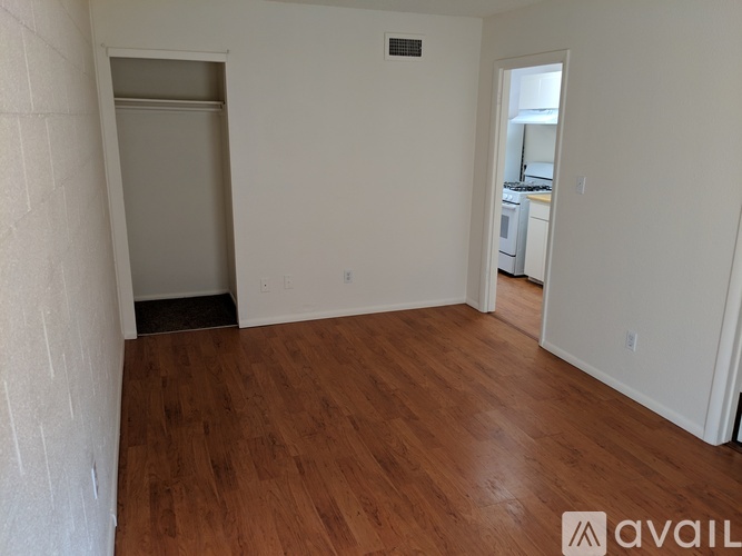 A room with wooden flooring and white walls, with a doorway leading to another room.