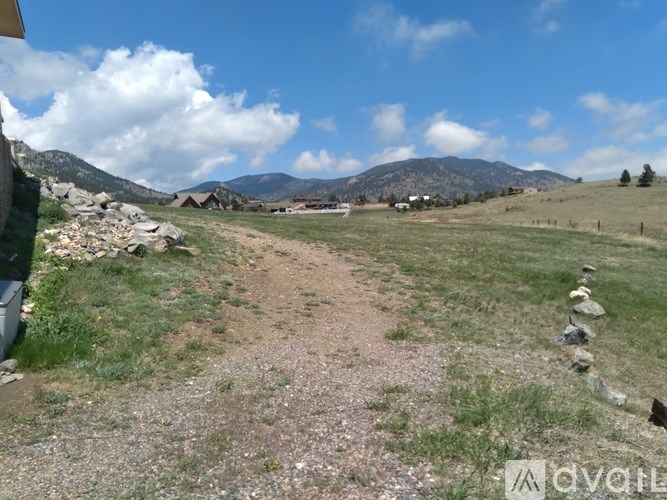 A dirt path leads through a grassy field with a stone wall on the right and mountains in the distance.