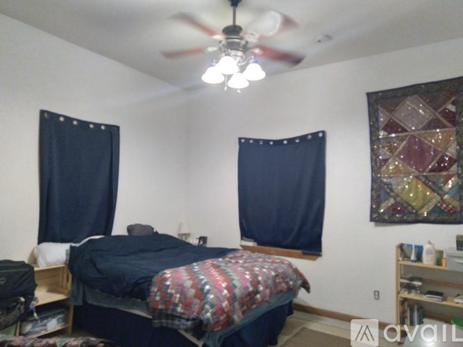 A bedroom with a bed, a ceiling fan, and a window with curtains.