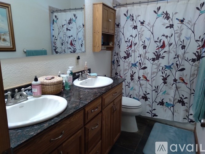 A bathroom with a floral shower curtain and wooden cabinets.