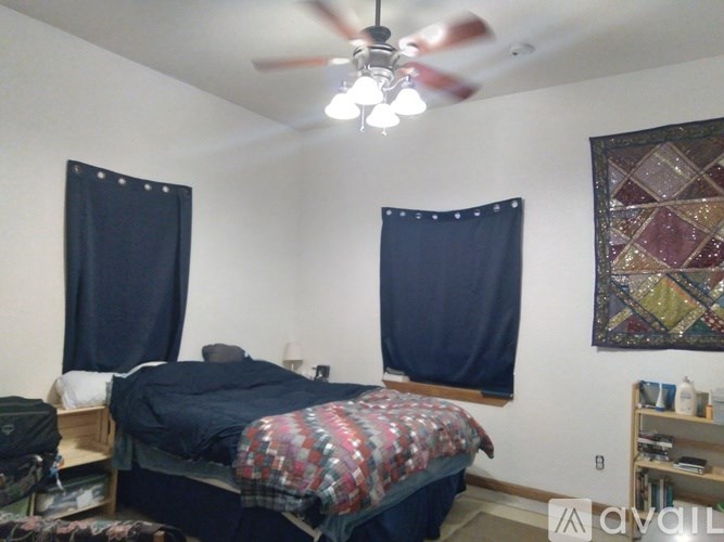 A bedroom with a bed, a ceiling fan, and a quilt on the bed.