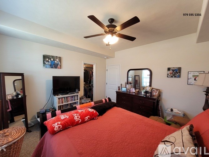 A bedroom with a red bedspread and a ceiling fan.