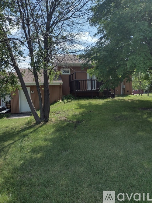 A house with a brown roof and a white door is surrounded by a green lawn.