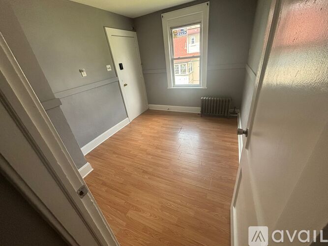 A room with wooden flooring and a window with a view of a building outside.