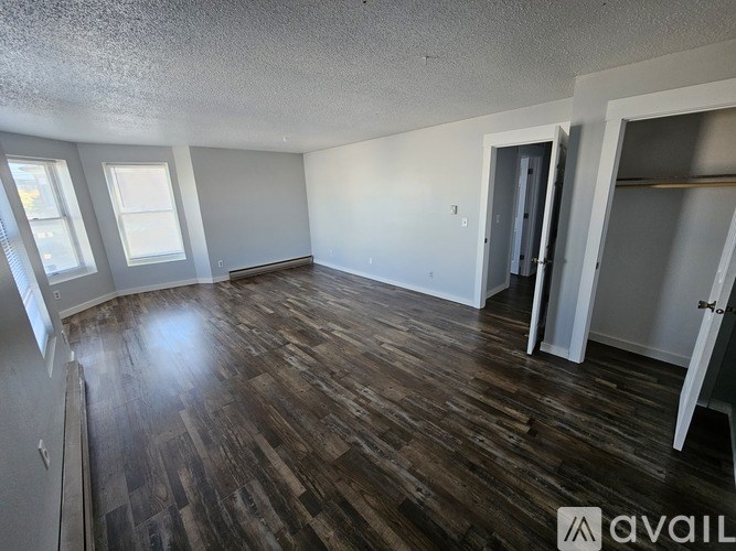 A room with wooden flooring and white walls, with a window on the left side.