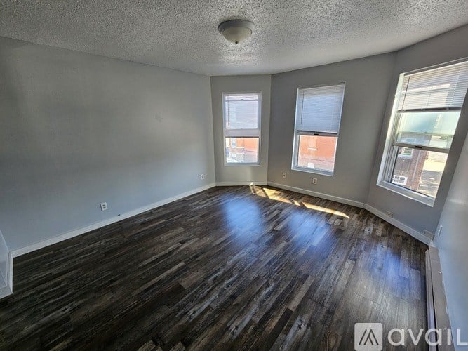 A room with wooden flooring and three windows.