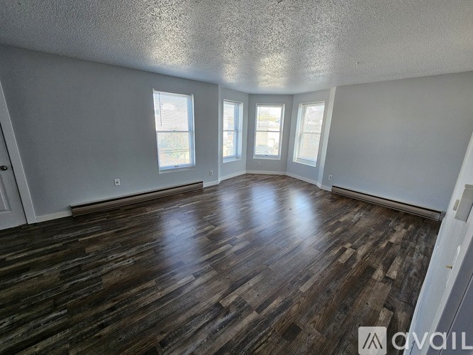 A room with wooden flooring and three windows.