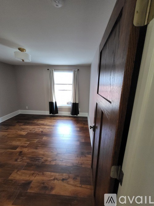 A room with wooden flooring and a window with curtains.