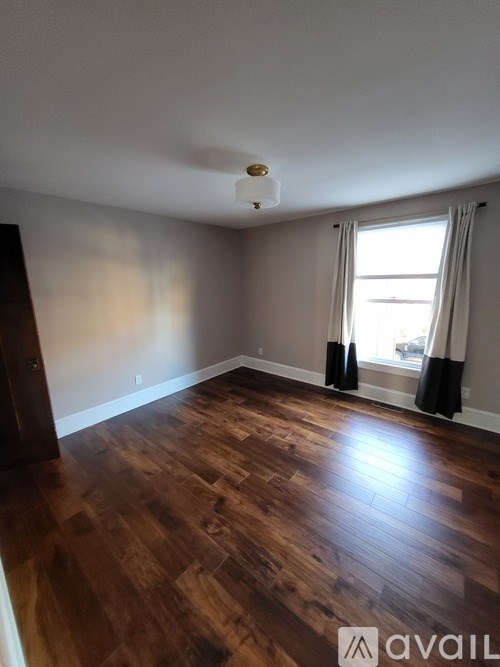 A room with wooden flooring and a window with curtains.