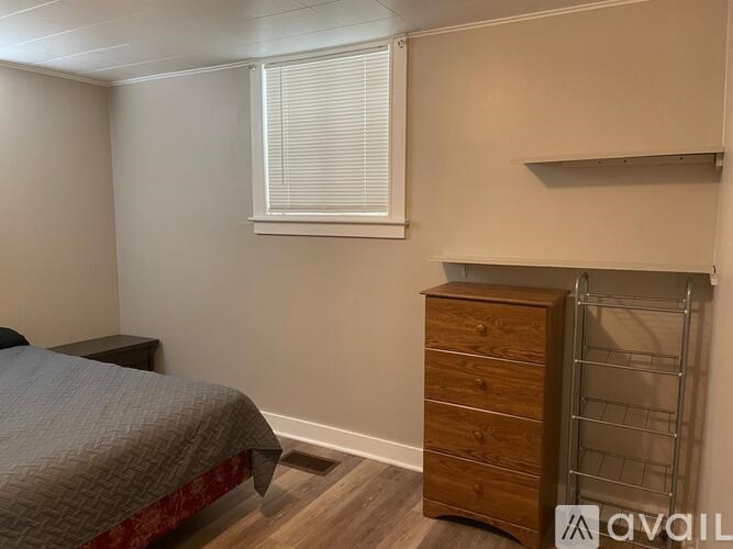 A bedroom with a bed, wooden dresser, and a wall-mounted shelf.