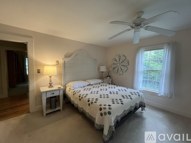 A bedroom with a large bed, a ceiling fan, and a window with white curtains.