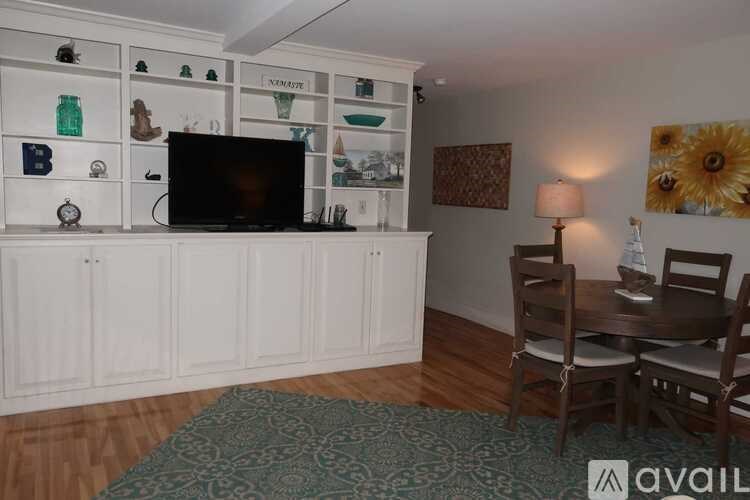 A living room with a television, a table with chairs, and a shelf with various items.