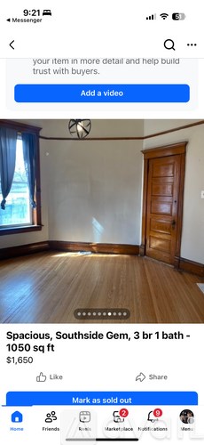 A room with wooden flooring and a large window with curtains.