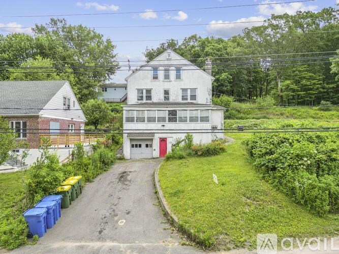 A white house with a red door is situated in a green area with a gravel road leading to it.