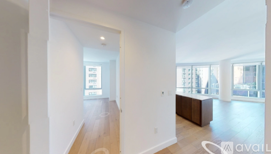 A spacious room with wooden floors and white walls, with a large window on the right side.