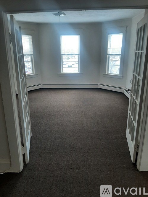 A room with a carpeted floor and three windows.