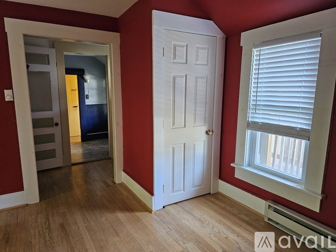 A room with a white door, a window with blinds, and a wooden floor.
