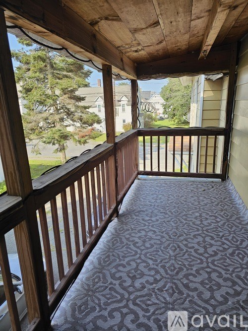 A wooden balcony with a carpeted floor and a view of a house and trees.