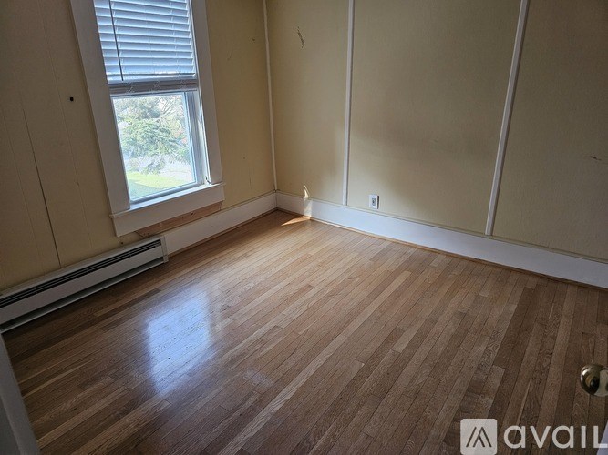 A room with wooden flooring and a window with blinds.