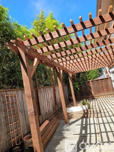A wooden pergola with a lattice top is over a patio.