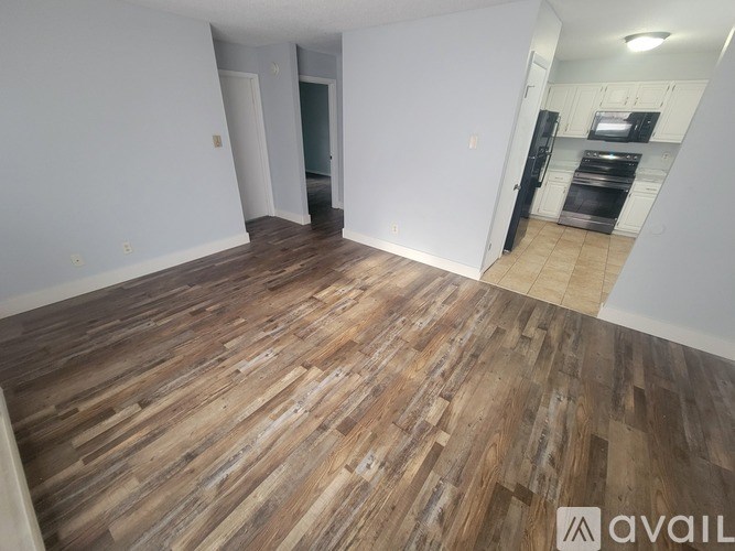 A room with wooden flooring and a kitchen area in the background.