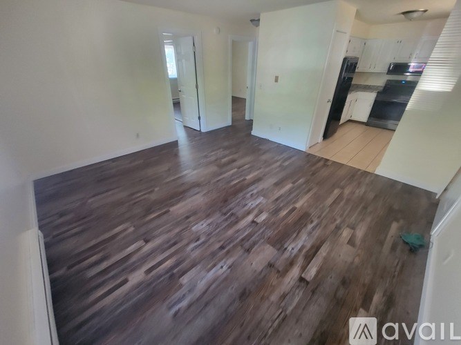 A room with wooden flooring and a kitchen area in the background.