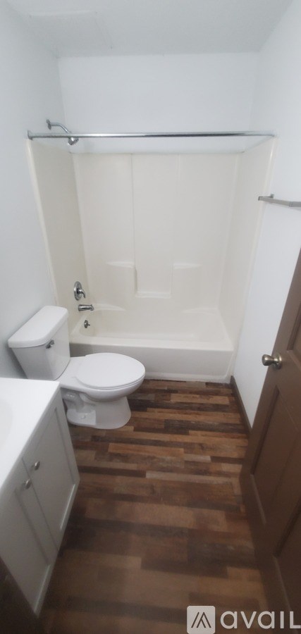 A bathroom with a toilet, a tub, and a wooden floor.
