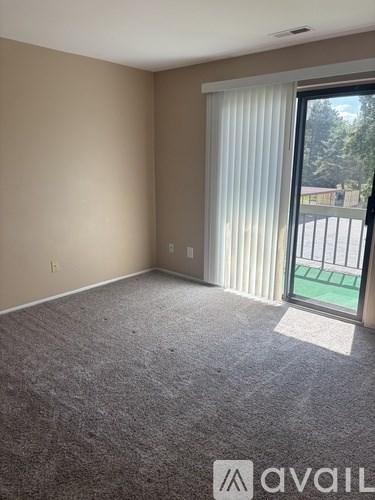 A room with a carpeted floor and a sliding glass door leading to a balcony.