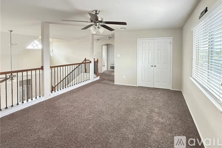 A spacious room with a carpeted floor, a ceiling fan, and a staircase with a railing.