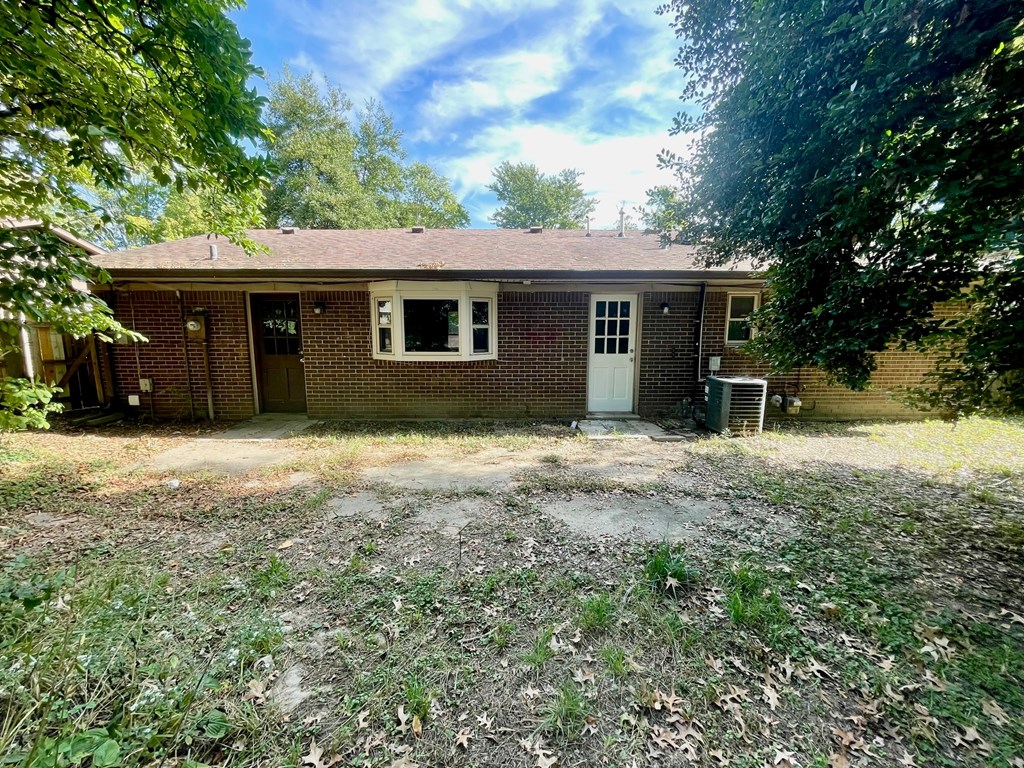 A small brick house with a white door and windows surrounded by trees.
