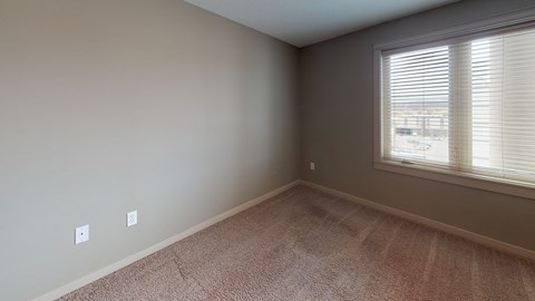 A room with a carpeted floor and a window with blinds.