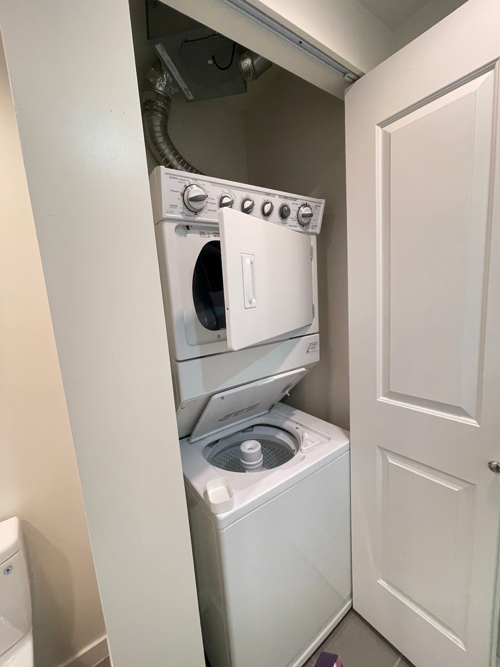 A white dryer and washer are stacked on top of each other in a small laundry room.