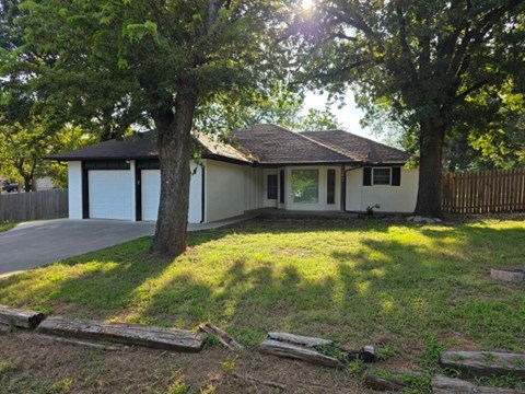 A house with a white garage door is surrounded by trees.