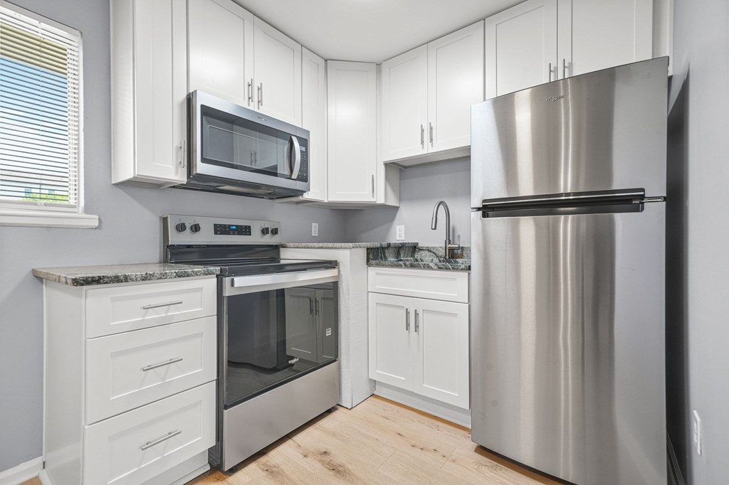 A kitchen with a stainless steel refrigerator, microwave, oven, and cabinets.
