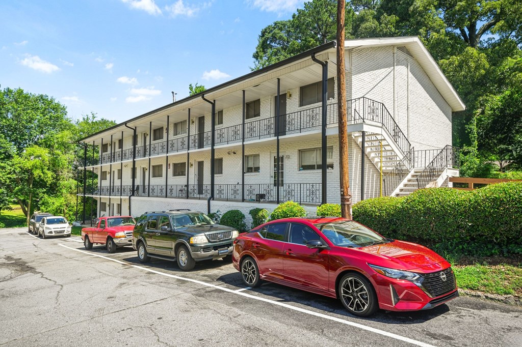 A red car is parked in front of a white apartment building.