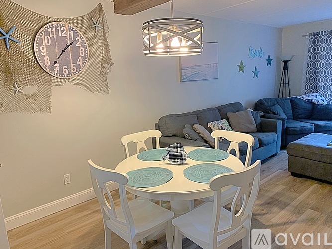 A dining room with a white table and chairs, a clock on the wall, and a couch in the background.