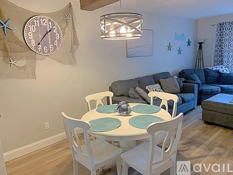 A dining room with a white table and chairs, a clock on the wall, and a couch in the background.