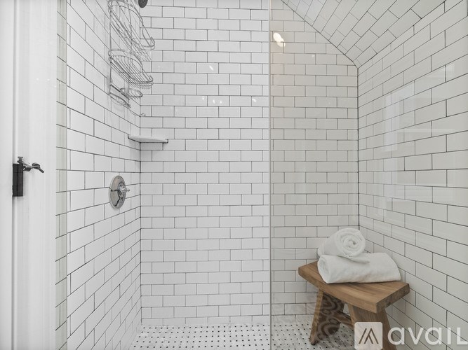 A white tiled bathroom with a wooden stool and towel.