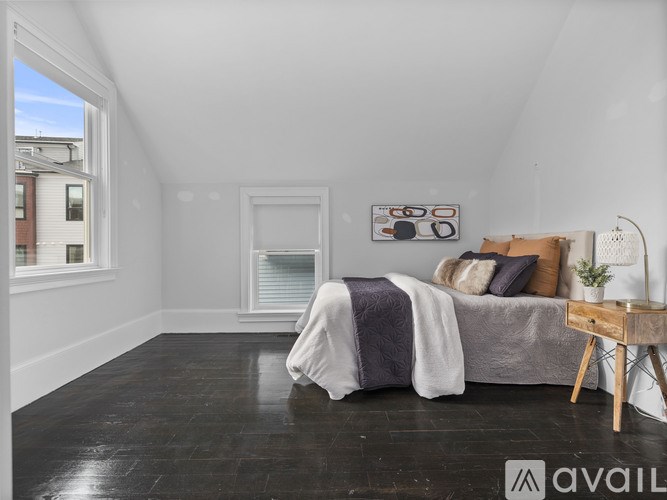 A bedroom with a bed, pillows, a blanket, a small table, and a window.
