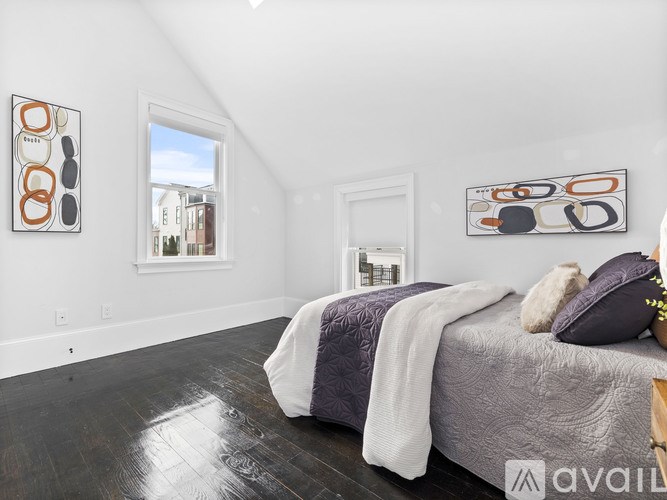 A bedroom with a bed, pillows, and a blanket with a window and artwork on the wall.