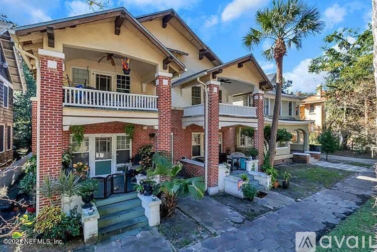 A red brick house with a balcony and a tree in front.