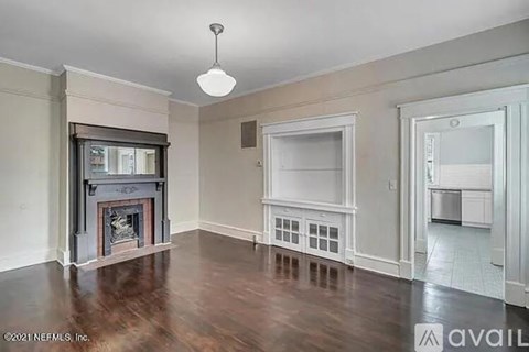 A living room with a fireplace and a kitchen in the background.