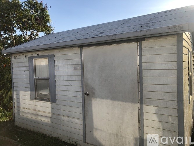 A small white building with a door and a window is available for rent.