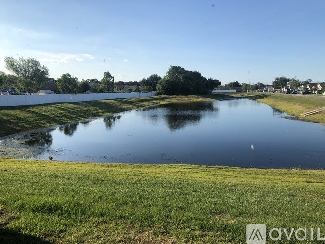 A calm lake surrounded by green grass and trees under a clear blue sky.